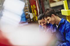 Male and female operator working together. Smiling. Caucasian man and Asian woman. Tech environment. Factory. Primary color white. Secondary color blue.