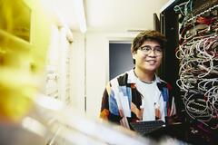 Smiling man holding an tablet standing in a servers room.