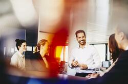 Business men and women in an office having a meeting. Primary color: red.