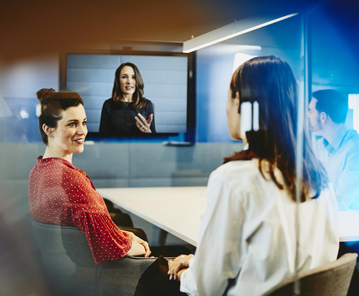 Two business women and a man in an office having a Hangout. Primary color: blue.