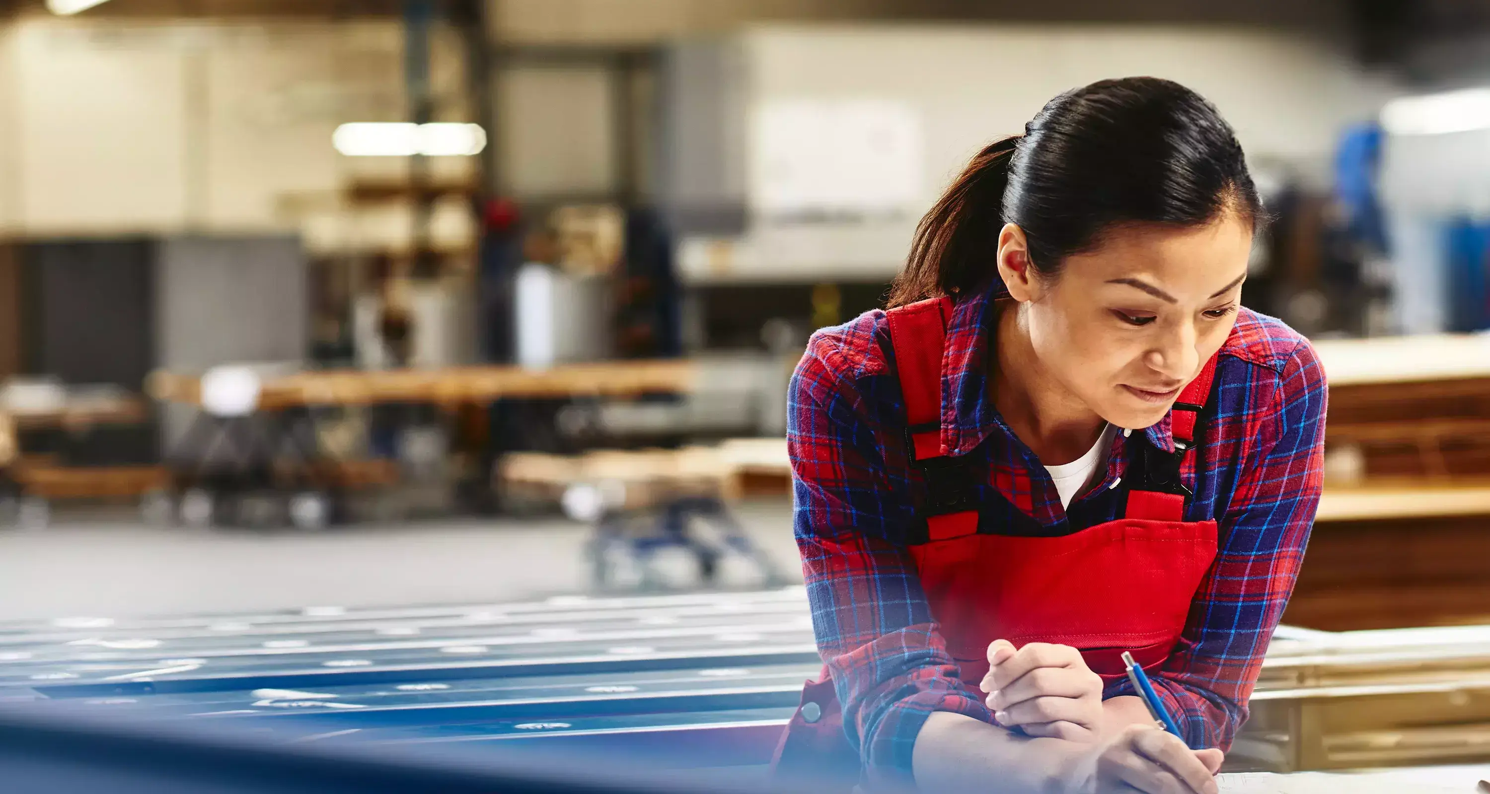 Womale wearing a red overall writing on a paper in a production site/factory.
