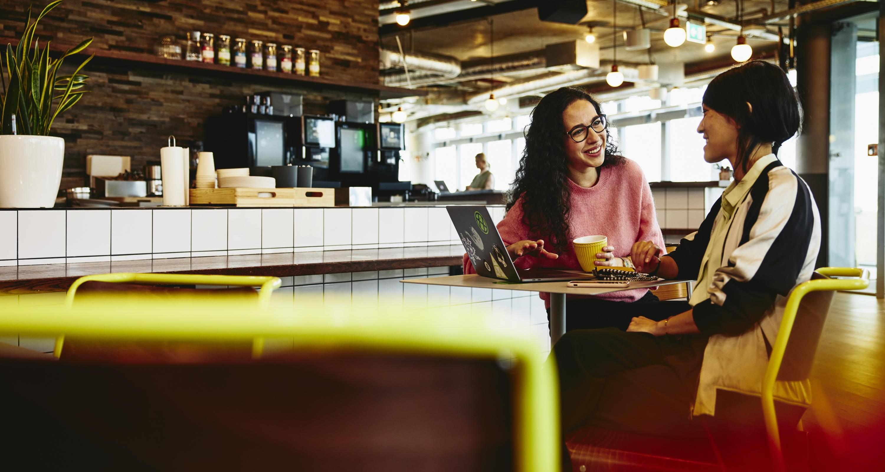 Two woman sitting in restaurant having a converstation, looking at laptop, smiling.