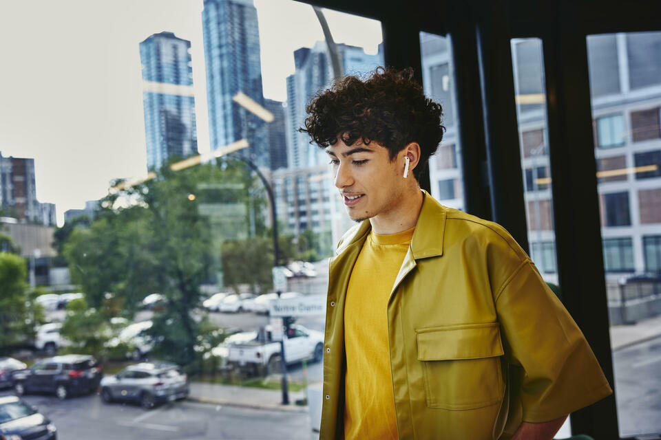 Male in yellow shirt, width earphones, standing at a window looking down